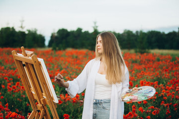 Woman artist painting in poppy field on sunny day