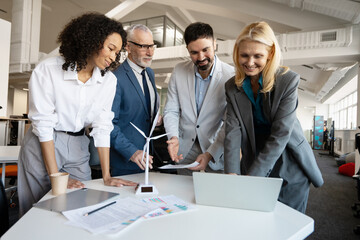 Business people discussing green energy project with miniature wind turbine in modern office