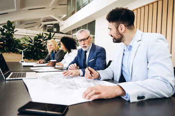 Businessmen and businesswoman working together on blueprint in modern office