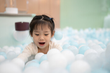 Joyful girl laughing in ball pit at indoor playground