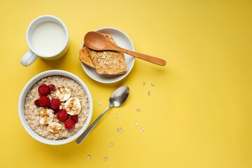 Top view on bowl of oatmeal with cup of milk on yellow background