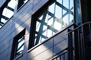 Glass windows on concrete loft wall with black metal external structure of office building in modern industrial style with sunlight and shadow on surface