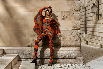 Beautiful model in colorful jumpsuit with butterfly flowing sleeves sensually poses in the city on...