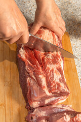 A cook's hand cuts raw pork neck with a knife for cooking. Close-up