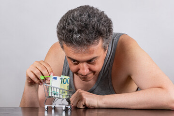Conceptual story about poverty with a grey-haired middle-aged man, 100 euro bill and miniature...