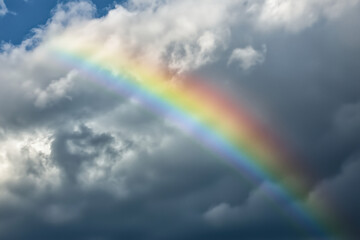 Natural rainbow arching across a cloudy sky enhanced by soft lighting effects during the day