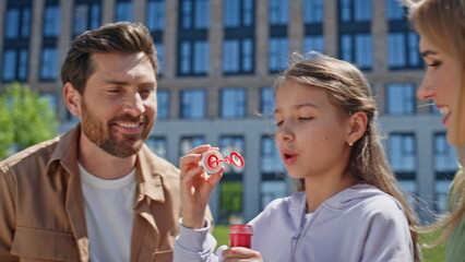 Playful family blowing soap bubbles on weekend picnic meadow together closeup
