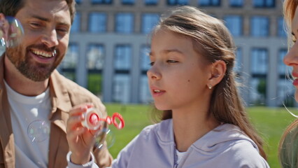 Cheerful girl playing soap bubbles at greenery neighbourhood picnic closeup