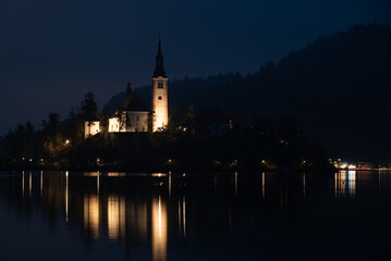 Obraz premium Assumption of mary pilgrimage church on bled island reflecting on lake bled at night. Slovenia
