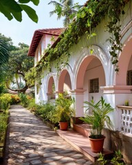 Fototapeta premium Goan heritage house with archways, hanging vines, red tile roof and tropical garden path in sunlight