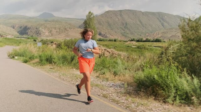 On a cloudy summer day, an overweight girl in sportswear runs along a mountain road, tracking her heart rate on her smartwatch. Despite heavy breaths and stifling air, she maintains pace and pushes on