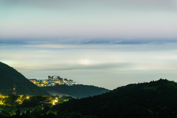A university stands illuminated atop Datun Mountain, Taipei, Taiwan, surrounded by mist and clouds on a spring night. The serene and mystical atmosphere is captured beautifully in this image.