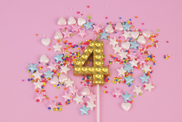 Gold birthday candle and sprinkles on pink background. Number 4.