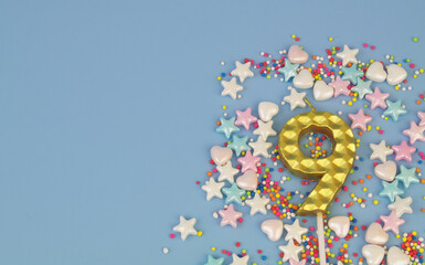 Golden birthday candle and colorful sprinkles on blue background. Number 9. Copy space for text.