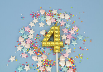 Gold birthday candle and many colorful sprinkles on blue background. Number 4.