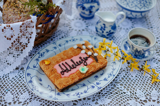 Easter braekfast table with mazurek cake, wicker basket, porcelain, coffee, flowers and vintage tablecloth 