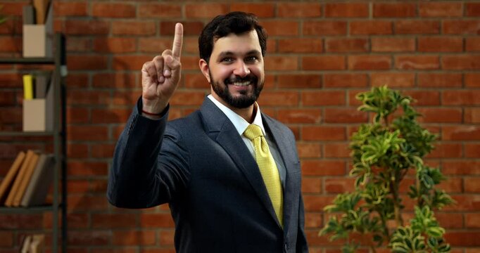 Showing numbers using fingers with confident expression, Indian Asian bearded ceo businessman in formal corporate attire demonstrating finger counting while standing in cozy office against brick wall