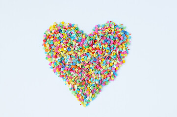 Multicolored confectionery cakes sprinkles laid out in the shape of a heart on a white background.