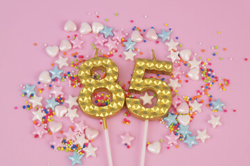 Gold birthday candles and many colorful sprinkles on pink background. Number 85.