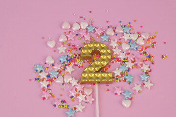 Gold birthday candle and sprinkles on pink background. Number 2.	