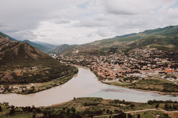 Two rivers meet by an ancient town nestled in the Georgian mountains under a cloudy sky
