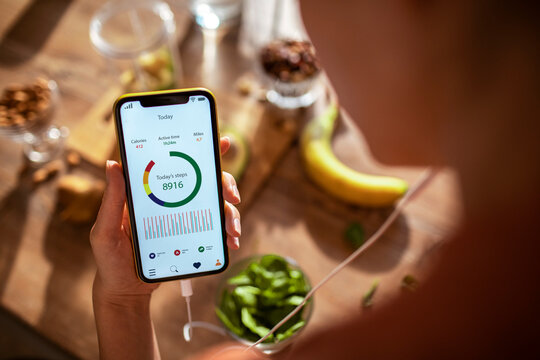 Woman tracking steps on smartphone fitness app surrounded by healthy food and fruits in kitchen