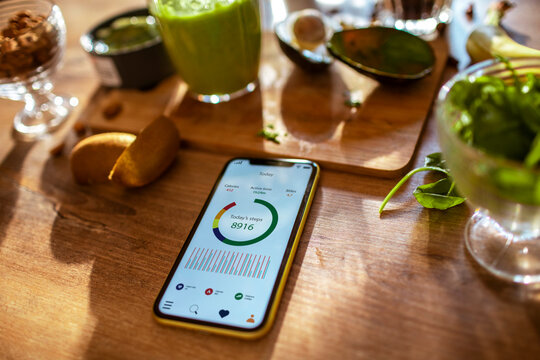 Healthy lifestyle tracking with smartphone app, green smoothie, and fresh fruits on kitchen table