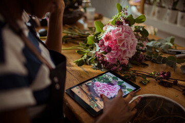 Florist arranging pink flowers while referencing photo on digital tablet