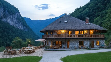A rustic building with a thatched roof near forested mountains