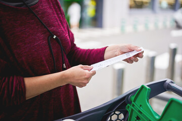 Woman checking shopping receipt next to cart outdoors
