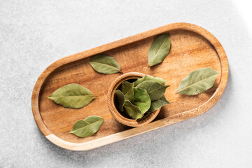 Fresh bay leaves arranged elegantly in a wooden tray on a gray background