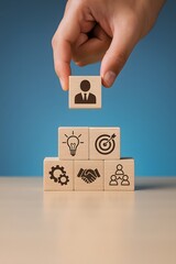 Stack of wooden blocks showing business icons being arranged in a pyramid. Concept of leadership, strategy, goal setting, teamwork, and organizational growth.