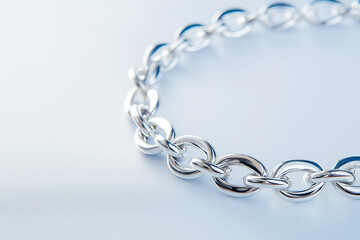 Obraz premium Closeup of a shining silver chain on a textured light background. Elegant silver chain captured in a detailed closeup with bright lighting on plain blue background.