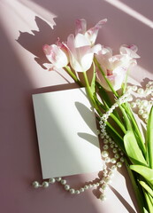 Greeting card mockup and pink tulip flowers and pearl necklace on pink background top view flatlay. Blank mock up with copy space.Mother's day, birthday, wedding concept.