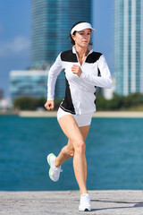  Young woman running jogging by Biscayne Bay with Miami condominium towers in background