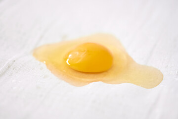 Bright yellow egg yolk rests on textured white surface. Soft lighting highlights yolks glossy texture, contrasting with absorbent background. Close-up captures culinary simplicity