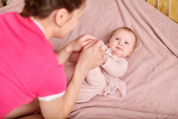 Smiling adult woman with brown hair interacts with baby girl. Baby lies on pink blanket. Warm lighting enhances soft pink colors, creating cozy atmosphere