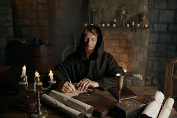 Portrait of medieval monk writing historic manuscripts at table