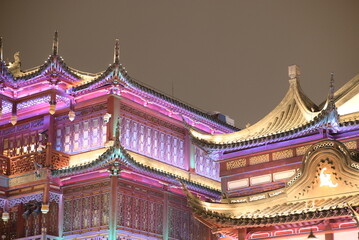 Colorful nighttime photo of Asian-style architecture. The building is decorated with pink, yellow, and purple lights on the ornate rooftop.