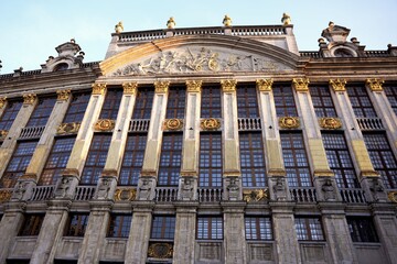 Detailed view of a golden baroque guildhall at Grand Place, Brussels, featuring large windows, carvings, and decorative sculptures. 