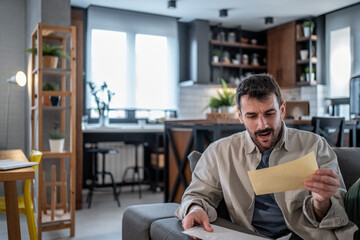Shocked man reading negative news in a letter at home