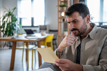 Fototapeta premium Pensive entrepreneur reading important documents in modern office