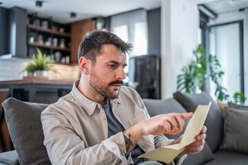 Worried man reading a letter at home on the sofa