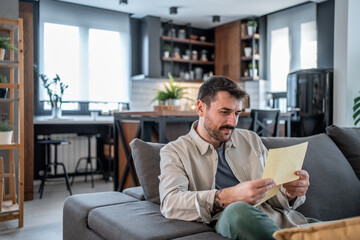 Focused man reading important documents on sofa in modern apartment