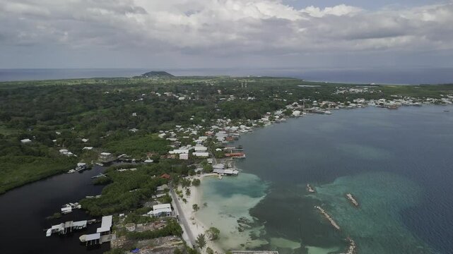 Drone flies backwards high over isthmus next to Chepes Beach in Utila, Honduras on partially cloudy afternoon