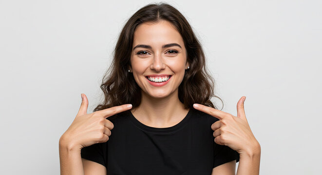 Joyful woman pointing at own smile cheeks happiness confidence grey background. Expressing happiness, self-joy, positive attitude concept.