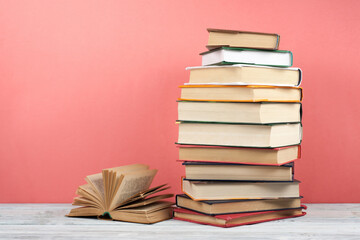 Open stacking book, hardback colorful books on wooden table, red, pink background. Back to school. Copy space for text. Education business concept.