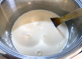 Foamy egg and milk mixture in a metal pot with a wooden spatula. Close-up of creamy texture, preparation for custard or sauce.