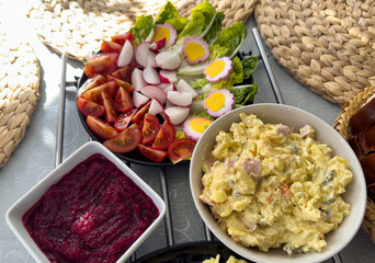 Close-up of traditional Easter sides: potato salad, beetroot puree, tomatoes, radishes, lettuce, and decorated eggs. Fresh and festive spring meal.