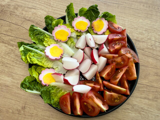Fresh spring vegetable platter with cherry tomatoes, radishes, lettuce, and flower-shaped decorated eggs. Bright and festive Easter side dish.
